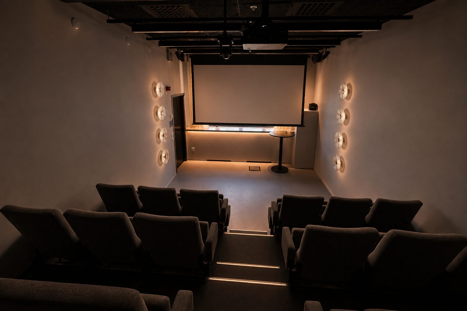 The front of the screening room, with the screen lowered and a standing table beside it